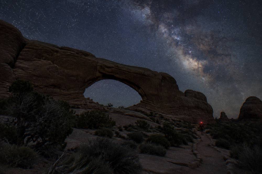 The Milky Way arching above silhouetted sandstone formations on a moonless night