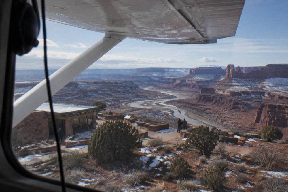 A small airplane wing above red rock canyons and a winding river