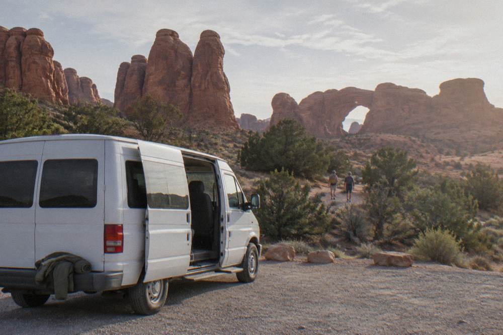 A shuttle van at a trailhead pullout beside tall red rock fins