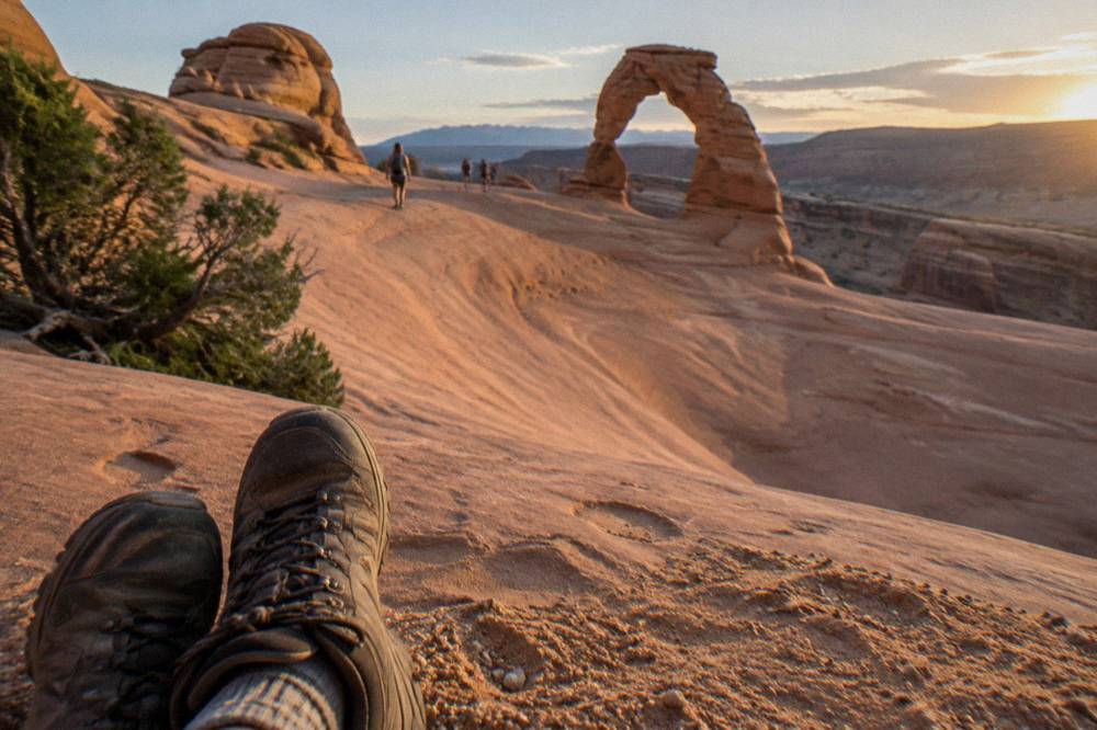 Sturdy hiking shoes standing on smooth red slickrock beside a sandy trail