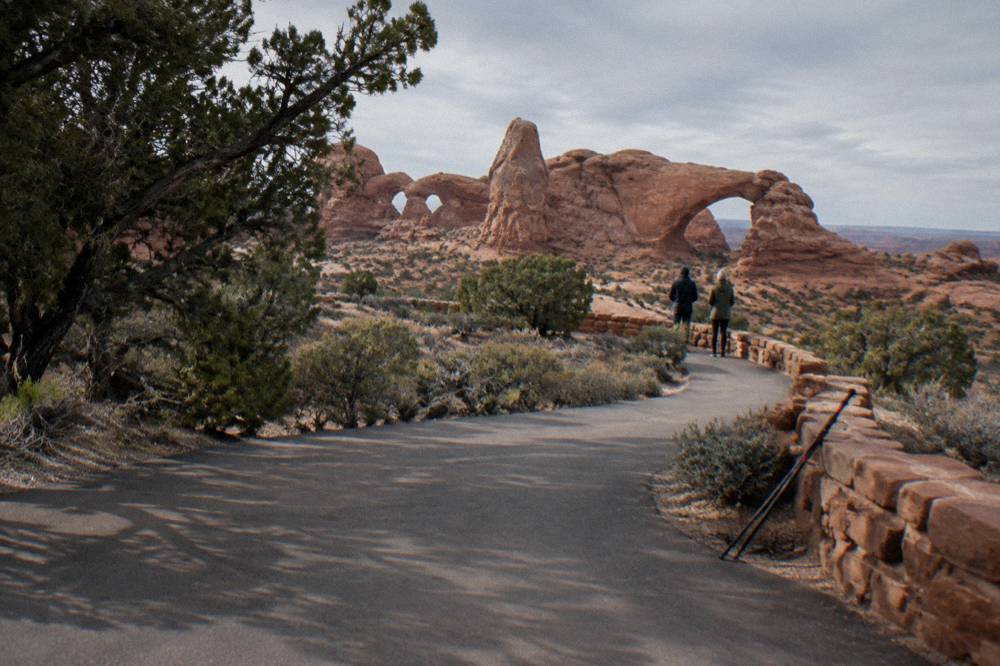 A shaded bench overlook at a paved viewpoint above wide red rock formations